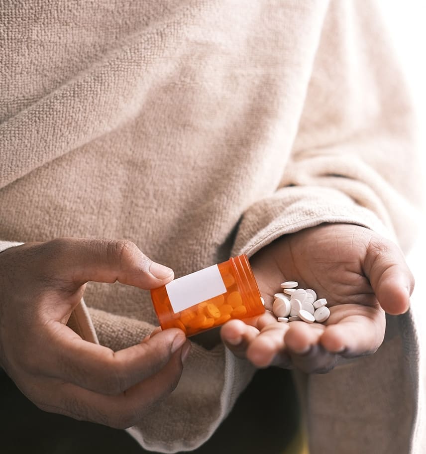 Close-up of a person's hands holding an open amber prescription bottle and a palmful of white pills
