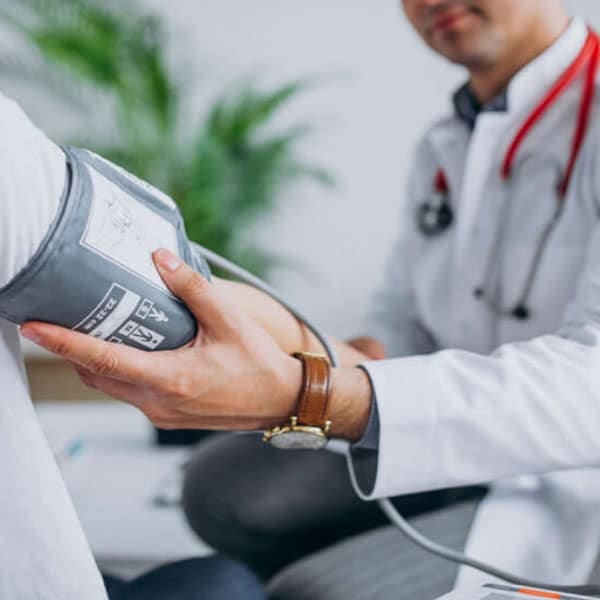 Doctor in a white coat measuring a patient's blood pressure with an arm cuff during a clinical exam