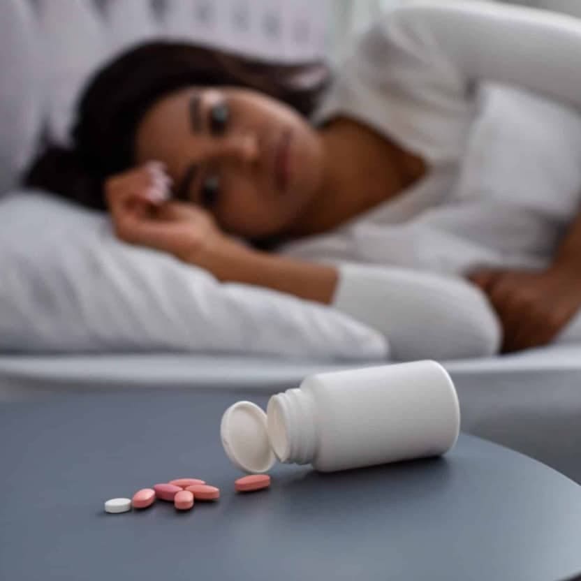Woman in bed beside spilled pills, representing severe and chronic alcohol use