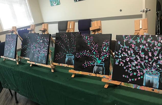 Row of completed art-therapy paintings displayed on wooden easels along a table in a treatment room