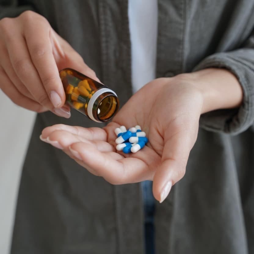 A person pouring blue-and-white capsules from an amber prescription bottle into their open palm