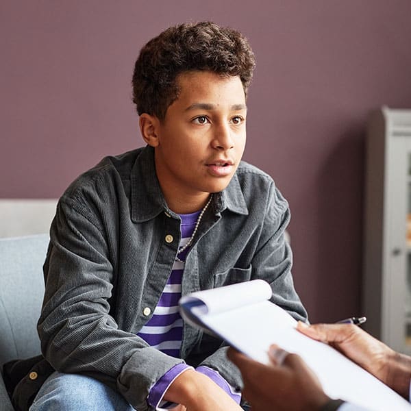 Adolescent boy speaking with a counselor who takes notes during a therapy session