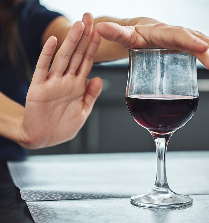 A person raising a hand to refuse a glass of red wine on a countertop, symbolizing the choice of sobriety