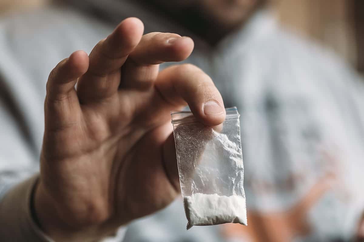 Close-up of a hand holding a small plastic baggie of white powder representing cocaine