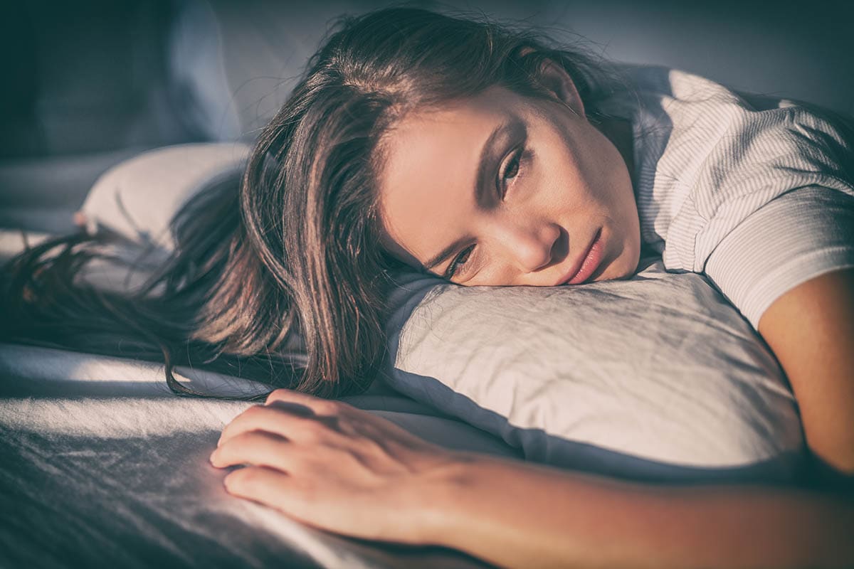 Young woman lying on a pillow in bed looking sad and withdrawn