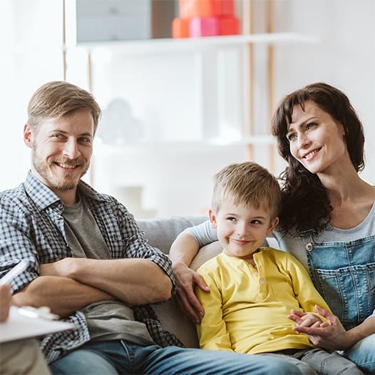 A man, young boy, and woman sitting together on a couch and smiling during a family therapy session