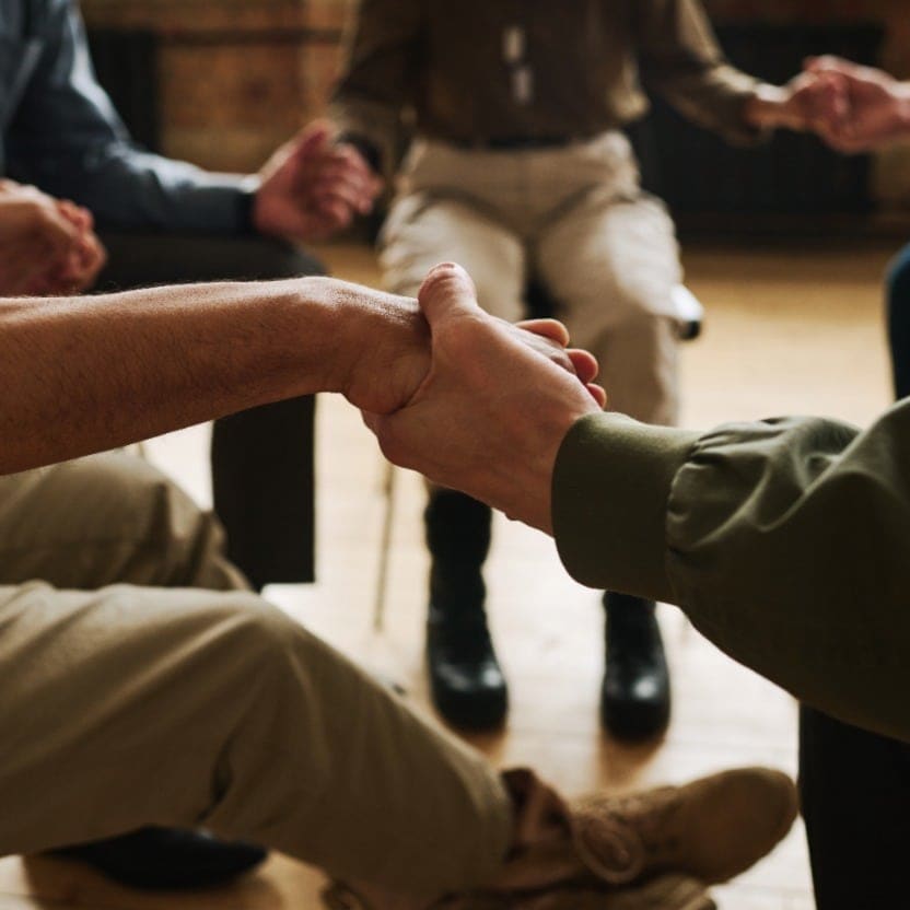 Two people clasping hands in support during a seated group therapy circle