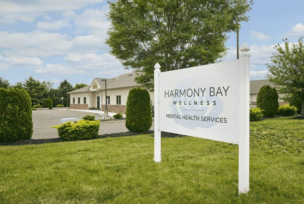 Exterior of a single-story behavioral health facility with a white lawn sign reading Harmony Bay Wellness Mental Health Services