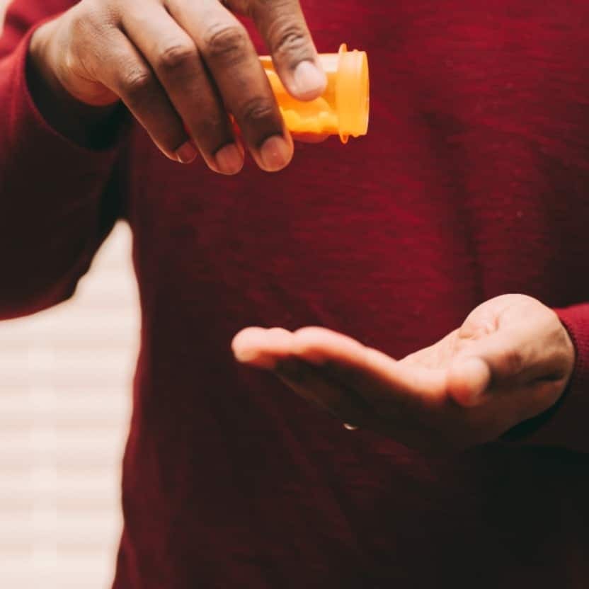 Person tipping pills from an orange prescription bottle into their open hand