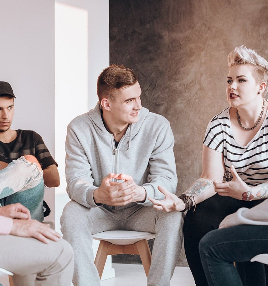 Young adults seated in a circle talking during a group therapy session in a bright room