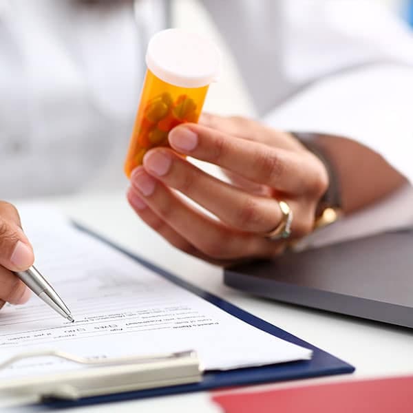 A clinician in a white coat holding an amber prescription bottle while writing on a clipboard