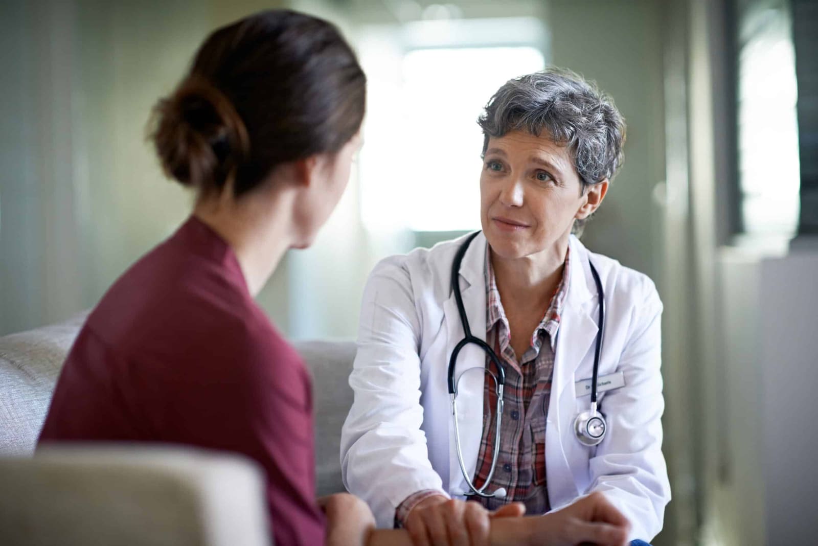 Female doctor in a white coat with a stethoscope speaking with a seated patient during a consultation