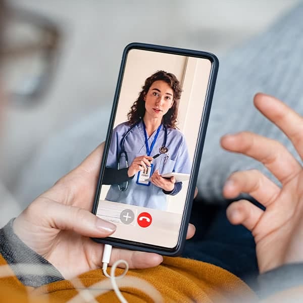 Patient on a video call with a clinician in scrubs via a smartphone telehealth app